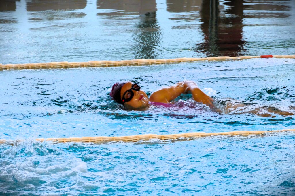 Zdjęcie przedstawia młodą pływaczkę biorącą udział w zawodach pływackich.