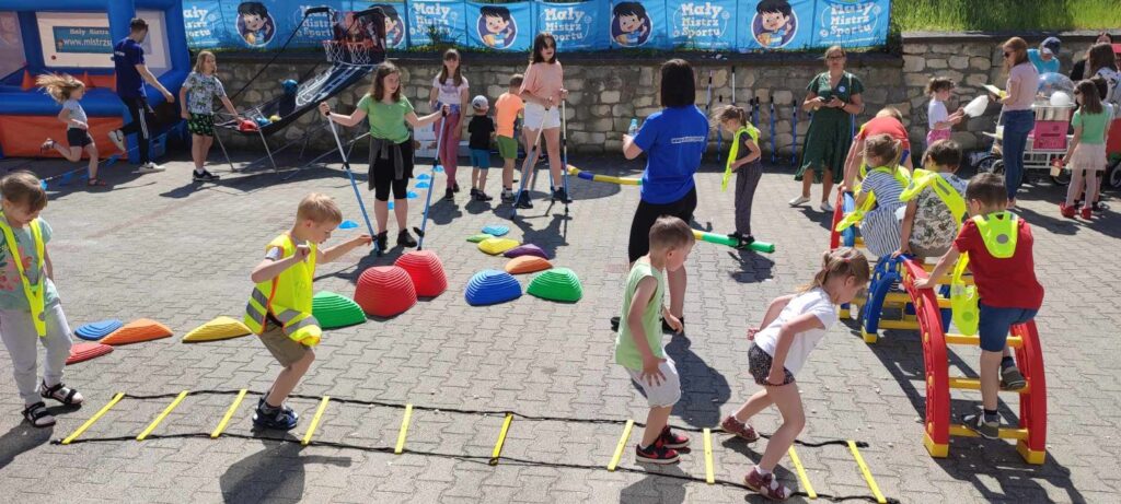 zdjęcie przedstawia szereg atrakcji sportowo rekreacyjnych i bawiące się dzieci